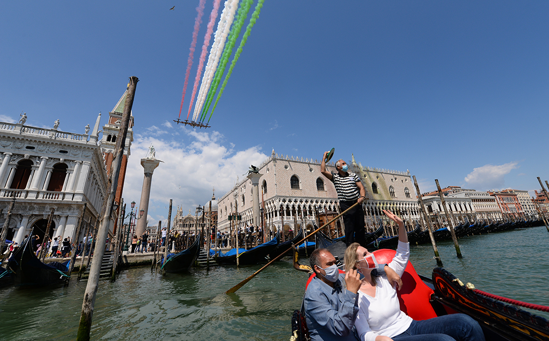 Em Veneza, na Itália, pessoas passeiam de gôndola e registram as acrobacias aéreas.